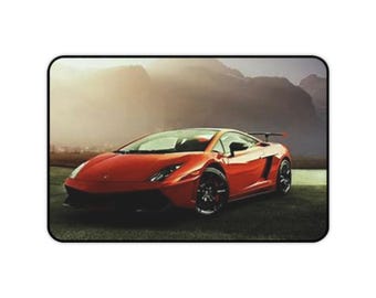 Può includere: Un'auto sportiva rossa con uno spoiler nero e ruote nere è parcheggiata su un'area erbosa con uno sfondo di montagna.