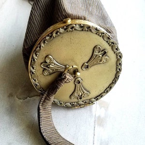 May include: A vintage, brown, fabric purse with a gold metal clasp and ornate design. The purse has a long, brown strap.