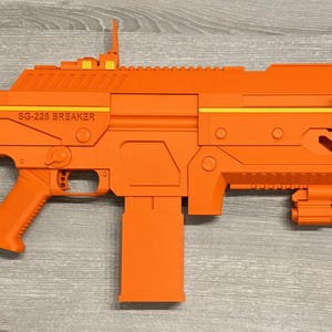 May include: A bright orange toy rifle featuring a rectangular magazine, a stock with circular cutouts, and a top rail with a sight. The side of the rifle is embossed with the text SG-225 BREAKER, accented by a thin horizontal yellow stripe.