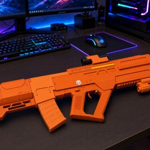 May include: A bright orange toy rifle featuring a tactical design with a detachable magazine, a top-mounted sight, and a small white skull icon printed on the side. The body includes the text AR-23 LIBERATOR and has a textured grip and stock.