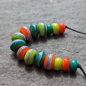 May include: A colourful necklace made of round beads with stripes of green, blue, yellow, and orange. The beads are strung on a black cord.