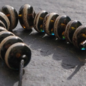 May include: A strand of black and white striped glass beads with a brown and blue iridescent sheen. The beads are strung on a black cord.