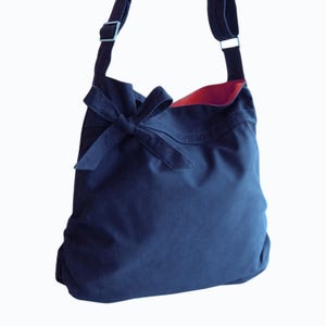 May include: A dark blue canvas tote bag with a large bow on the front. The bag has a red lining and a long adjustable strap.
