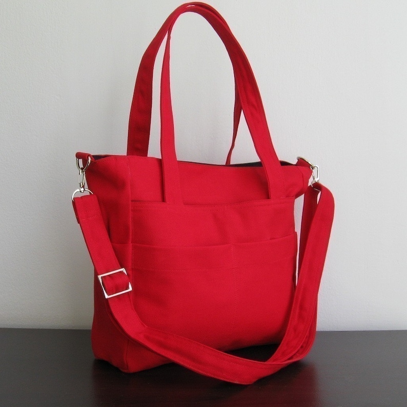 May include: A bright red tote bag with a long shoulder strap and multiple pockets. The bag has a zipper closure and two top handles.