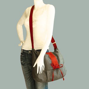 May include: A gray canvas messenger bag with a red stripe and a red bow. The bag has a long red strap.