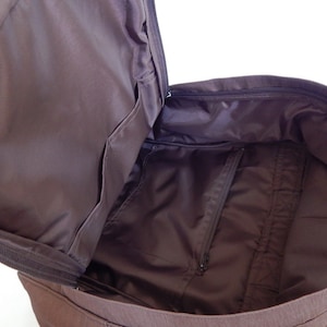 May include: A brown canvas backpack with a zippered main compartment and a smaller zippered pocket inside. The backpack is open and the interior is visible.