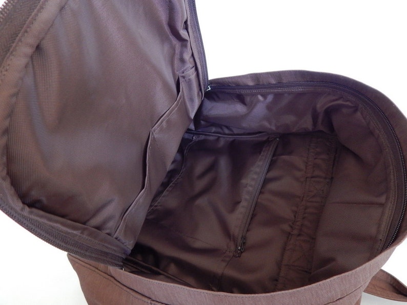 May include: A brown canvas backpack with a zippered main compartment and a smaller zippered pocket inside. The backpack is open and the interior is visible.