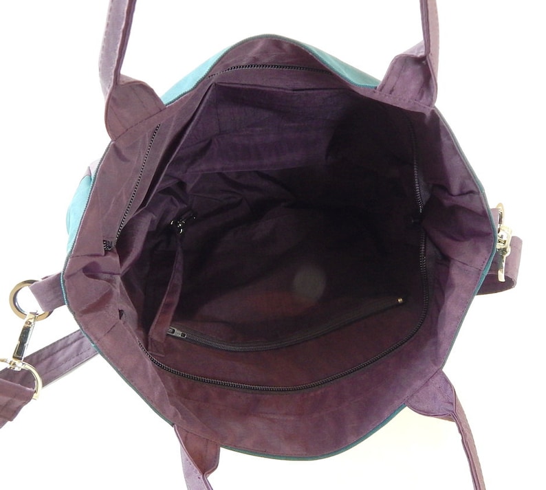 May include: A purple tote bag with a zippered pocket on the inside. The bag has a long strap and two shorter handles.