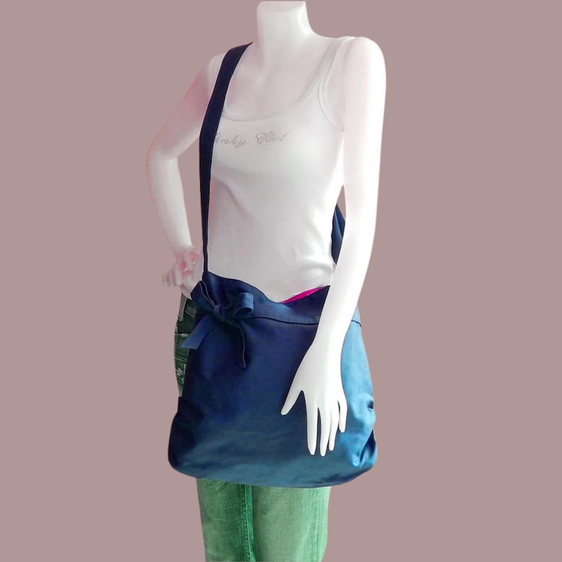 May include: A dark blue satin tote bag with a large bow on the front. The bag has a long strap and is worn over the shoulder.