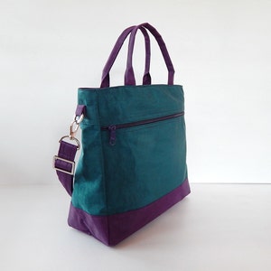 May include: A teal green tote bag with a purple bottom and a purple strap. The bag has a zippered pocket on the front.