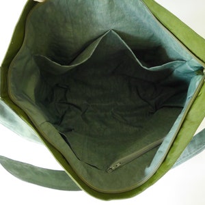 K&ouml;nnte beinhalten: Gr&uuml;ne Canvas-Tragetasche mit Rei&szlig;verschluss und mehreren Innentaschen. Die Tasche hat einen langen Riemen zum Tragen &uuml;ber der Schulter.