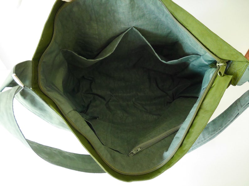 K&ouml;nnte beinhalten: Gr&uuml;ne Canvas-Tragetasche mit Rei&szlig;verschluss und mehreren Innentaschen. Die Tasche hat einen langen Riemen zum Tragen &uuml;ber der Schulter.