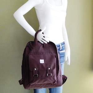 May include: A brown canvas backpack with a large front pocket and adjustable straps. The backpack has a small logo on the front pocket.