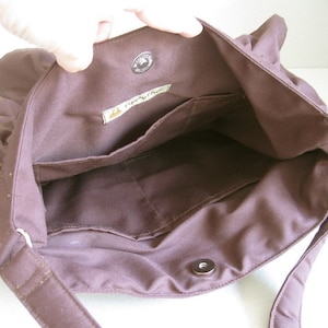 May include: The inside of a brown canvas bag with a zipper closure and a small pocket. The bag has a label that reads 'Simply Green'.