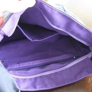 May include: A gray canvas tote bag with a purple lining. The bag has a zippered pocket and two open pockets inside.