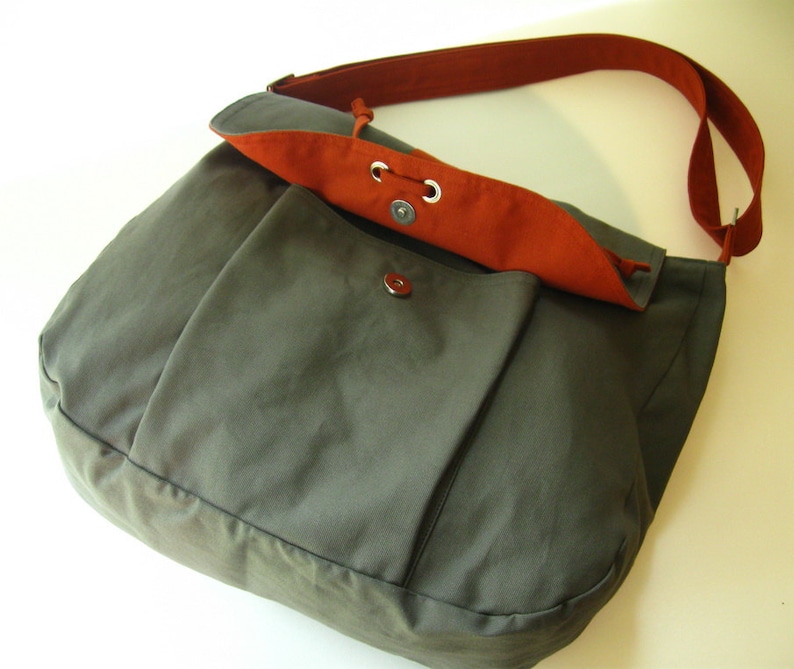 May include: A gray canvas messenger bag with a red flap and a drawstring closure. The bag has a long adjustable strap.