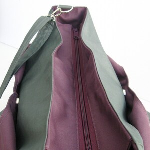 May include: A two-tone tote bag with a dark green exterior and a deep purple interior. The bag features a long, adjustable strap, a zipper closure, and silver-toned hardware. The bag's design is simple and functional, suitable for everyday use.