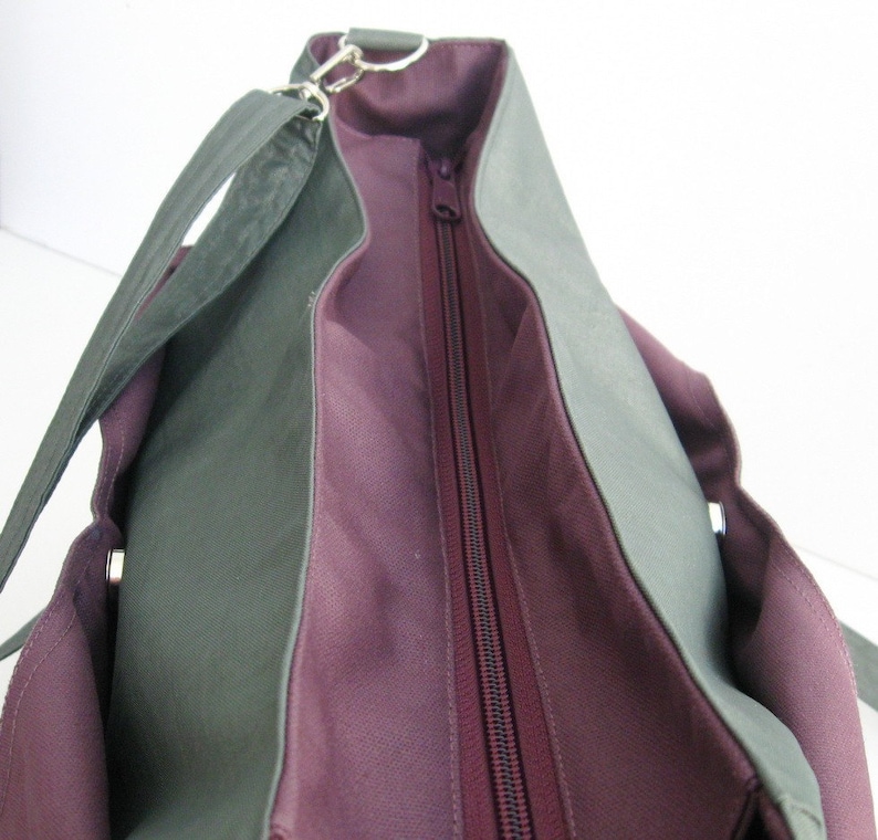 May include: A two-tone tote bag with a dark green exterior and a deep purple interior. The bag features a long, adjustable strap, a zipper closure, and silver-toned hardware. The bag's design is simple and functional, suitable for everyday use.