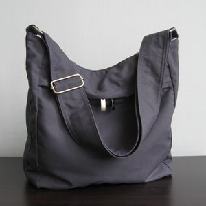 May include: A dark gray canvas tote bag with a long adjustable strap and a silver buckle. The bag has a flap with a small pocket on the front.