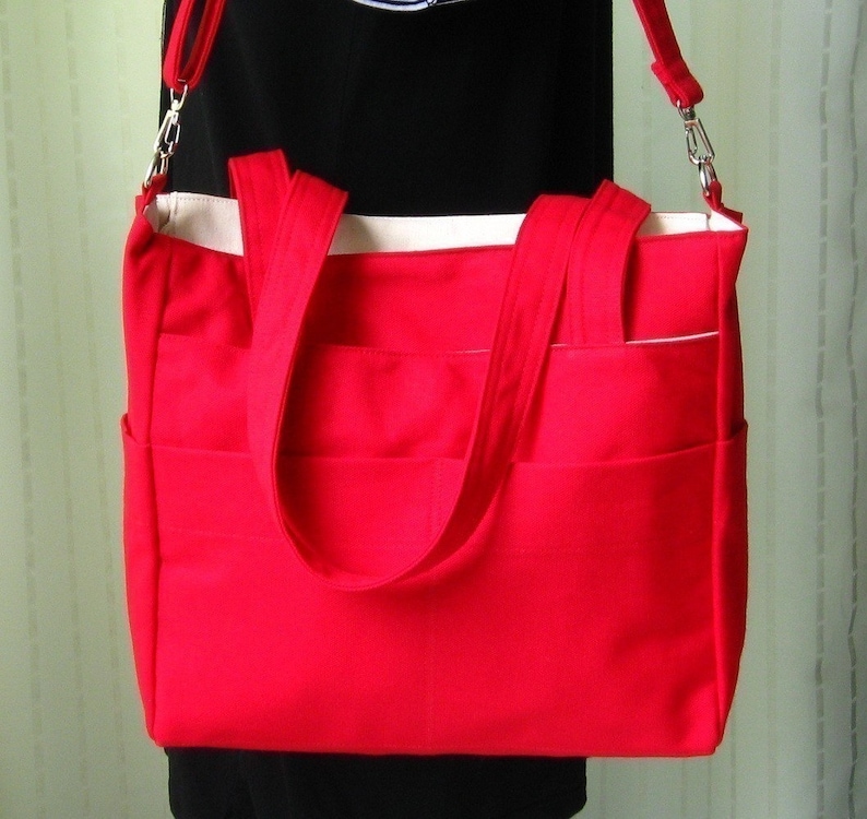 May include: A bright red tote bag with two top handles and a long shoulder strap. The bag has multiple pockets and a white lining.