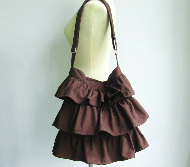 May include: A brown ruffled shoulder bag with a long strap.