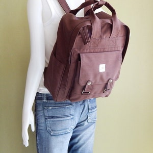 May include: A brown canvas backpack with a large front pocket and adjustable straps. The backpack has a simple design and is made of durable material.