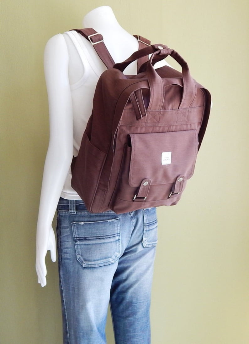 May include: A brown canvas backpack with a large front pocket and adjustable straps. The backpack has a simple design and is made of durable material.