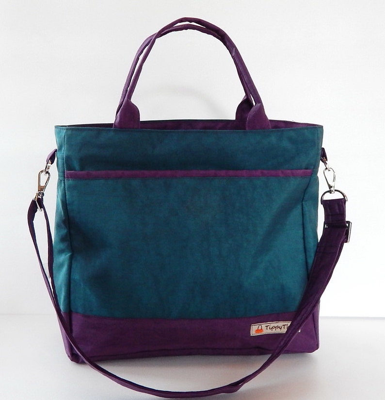 May include: A teal and purple tote bag with a shoulder strap and a small pocket on the front. The bag has a label that says "TippyT".