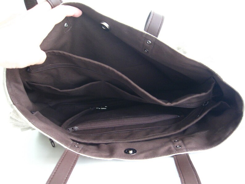K&ouml;nnte beinhalten: Beige Tragetasche mit braunem Innenraum und Griffen. Die Tasche hat mehrere Innentaschen, darunter Rei&szlig;verschlussf&auml;cher. Die Tasche ist offen und zeigt die Innenorganisation. Die Griffe sind dunkelbraun.