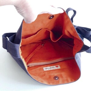 May include: A dark blue canvas tote bag with an orange lining. The bag has a zippered pocket and multiple interior pockets. The bag has a label that reads "The Happy Owl".