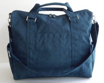 Peut inclure: Un sac de voyage bleu foncé avec une fermeture à glissière et une longue bandoulière. Le sac a une poche avant et une poignée supérieure.
