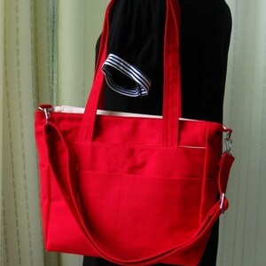 May include: A red tote bag with a long strap and a white lining. The bag has multiple pockets and is made of a durable fabric.