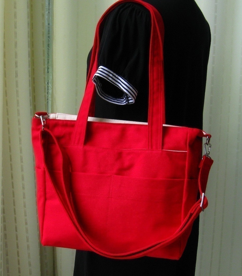May include: A red tote bag with a long strap and a white lining. The bag has multiple pockets and is made of a durable fabric.