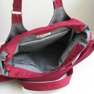 May include: A burgundy tote bag with gray lining and multiple pockets. The bag has a zippered main compartment and a long, adjustable shoulder strap. The interior features a small label with the text "Tippy Thai".