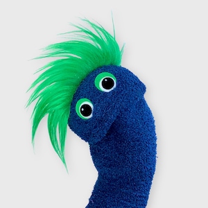 May include: A blue sock puppet with green hair and googly eyes. The puppet is made from a blue sock with a green fuzzy material for hair. The puppet has two large, black and white googly eyes.