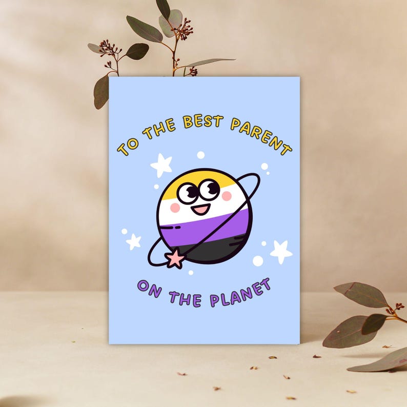 May include: A light blue greeting card with the text "TO THE BEST PARENT ON THE PLANET". The card features a cartoon planet with the non-binary pride flag colors and stars.