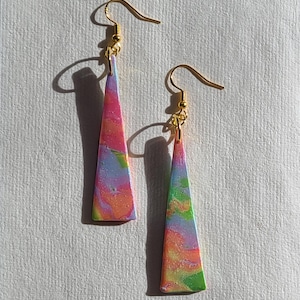 May include: A pair of dangle earrings with gold-colored hooks. The earrings have a triangular shape and are decorated with a colorful, swirled pattern of pink, orange, yellow, green, and blue.