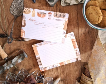 May include: A set of two recipe cards with a vintage kitchen theme. The cards are white with brown and orange illustrations of kitchen tools and ingredients. The top card has the word "Recipe" printed in brown and the bottom card has the word "Directions" printed in brown. The cards are on a wooden table with a bowl of cookies, a plate of cookies and brownies, and other kitchen items.