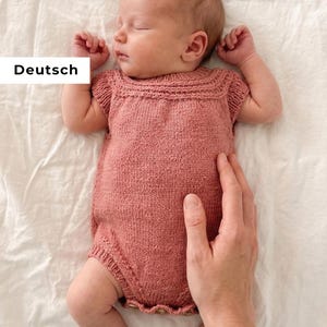 Puede incluir: Un bebé dormido con un pelele de punto rosa polvoriento con dobladillo festoneado. El pelele tiene mangas cortas y un escote cuadrado. La palabra "Deutsch" está en un rectángulo blanco en la esquina superior izquierda.