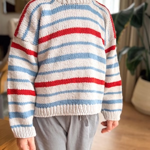 Pode incluir: Um su&eacute;ter de malha com listras horizontais vermelhas, azul claro e branco sujo. O su&eacute;ter tem gola redonda e mangas compridas. O fio &eacute; texturizado e a pe&ccedil;a parece ser feita &agrave; m&atilde;o.