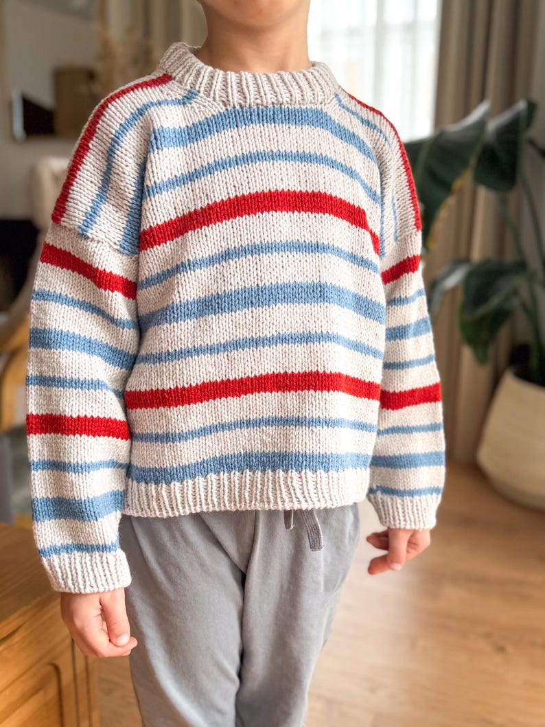Pode incluir: Um su&eacute;ter de malha com listras horizontais vermelhas, azul claro e branco sujo. O su&eacute;ter tem gola redonda e mangas compridas. O fio &eacute; texturizado e a pe&ccedil;a parece ser feita &agrave; m&atilde;o.