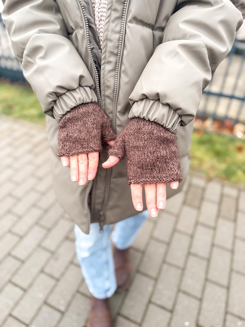 以下が含まれることがあります： 質感のあるニット糸で作られた茶色のフィンガーレスグローブ。手のひらと手の甲を覆い、指先を露出させるシンプルなデザインです。ニット素材には、かすかな霜降り調の風合いが見られます。