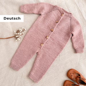 Puede incluir: Un pelele de bebé de punto rosa claro con mangas largas y botones de madera en la parte delantera. El pelele se combina con zapatos de bebé de cuero marrón. La palabra "Deutsch" es visible en la imagen.