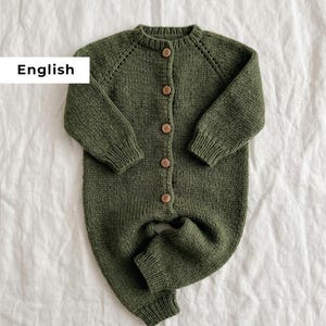 Puede incluir: Mono de bebé de punto verde oliva con botones de madera. El conjunto de una pieza tiene mangas y perneras largas, y un cuello redondo. La palabra "English" está en un rectángulo blanco en la esquina superior izquierda. Se muestra sobre una superficie blanca.
