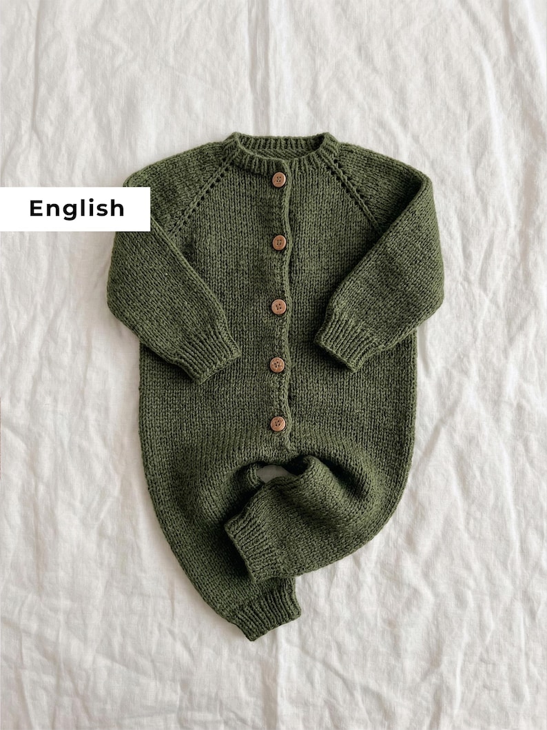 Puede incluir: Mono de beb&eacute; de punto verde oliva con botones de madera. El conjunto de una pieza tiene mangas y perneras largas, y un cuello redondo. La palabra "English" est&aacute; en un rect&aacute;ngulo blanco en la esquina superior izquierda. Se muestra sobre una superficie blanca.