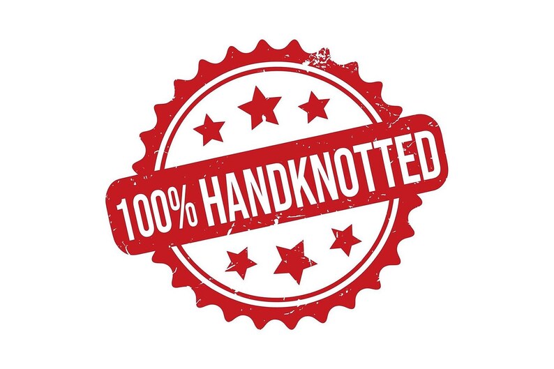 May include: A red stamp with the words "100% HANDKNOTTED" in white. The stamp is circular with a jagged edge and includes five stars. The text is in a rectangular shape that is angled across the circle.