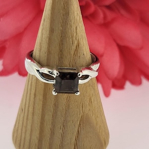 May include: A silver ring with a twisted band and a square, dark brown gemstone.
