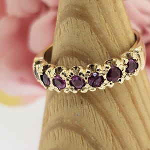May include: A gold band ring with a row of purple gemstones. The ring is on a wooden display stand.