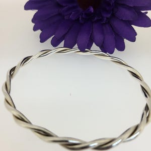 May include: A silver twisted bangle bracelet. The bracelet is made of two strands of silver wire that are twisted together to create a unique and stylish design.