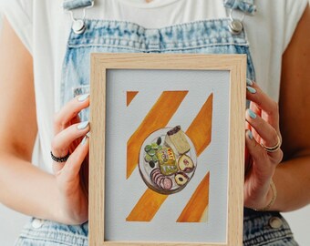 May include: A framed watercolour painting of a plate of food with a variety of items, including cheese, olives, salami, and fruit. The plate is on a background of orange and white stripes.